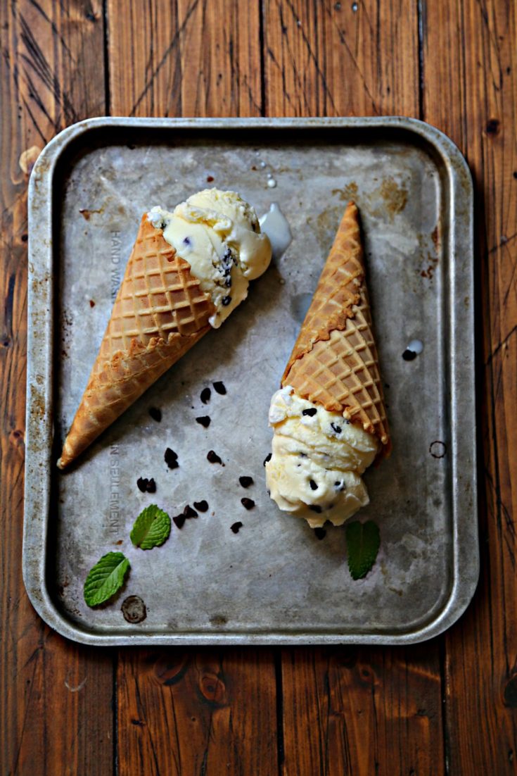 2 ice cream cones laying on baking sheet with scattered chocolate chips and fresh mint.