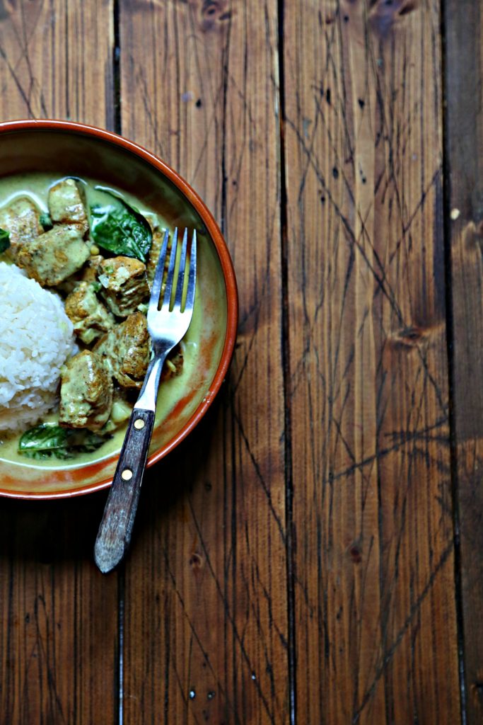 Brown bowl with ball of white rice and coconut curry chicken. Fork in bowl.