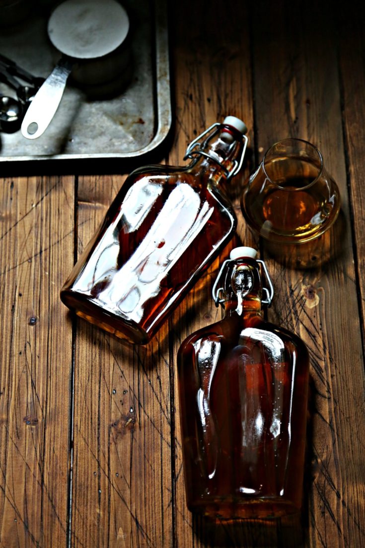 Glass Bottle with stopper of homemade amaretto with small white bowl of brown sugar in background via Bell'Alimento
