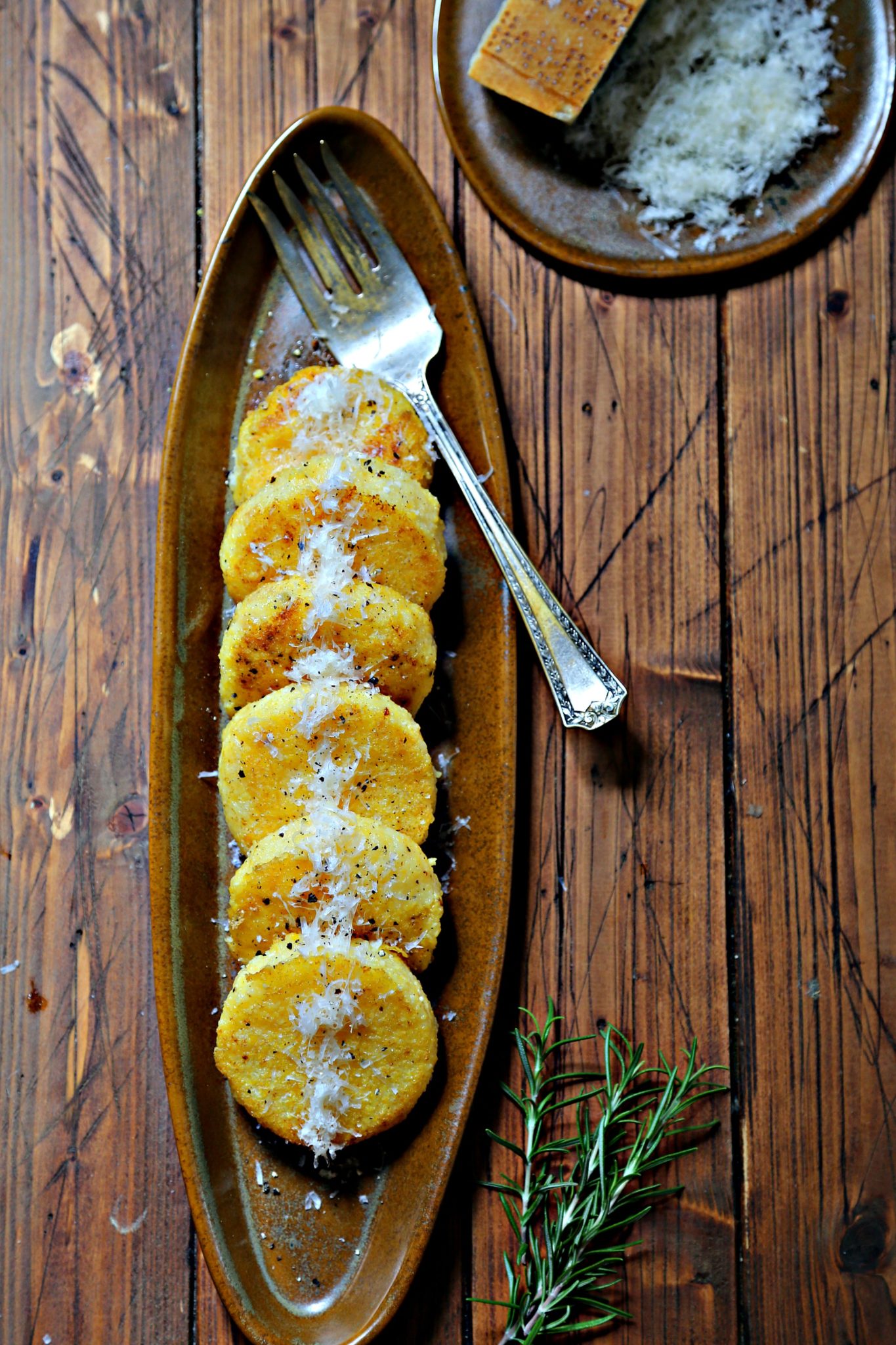 Polenta Cakes on brown platter with cheese and wood background via bell'alimento