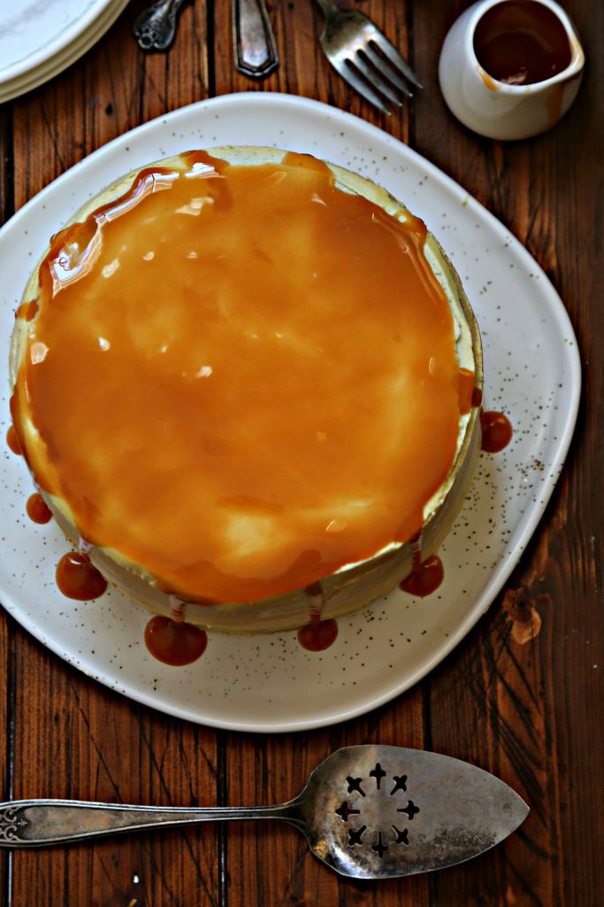 cake with caramel dripping off top on white plate. Serving utensil in front of cake. 