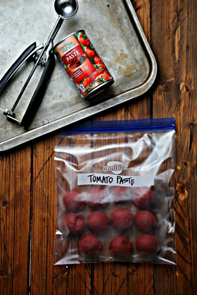 frozen tomato paste in freezer bag. Can of tomato paste and scooper on baking sheet in background.