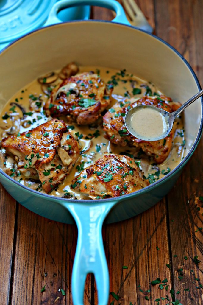 chicken with mushroom cream sauce in blue pot with spoon ladling sauce out. 