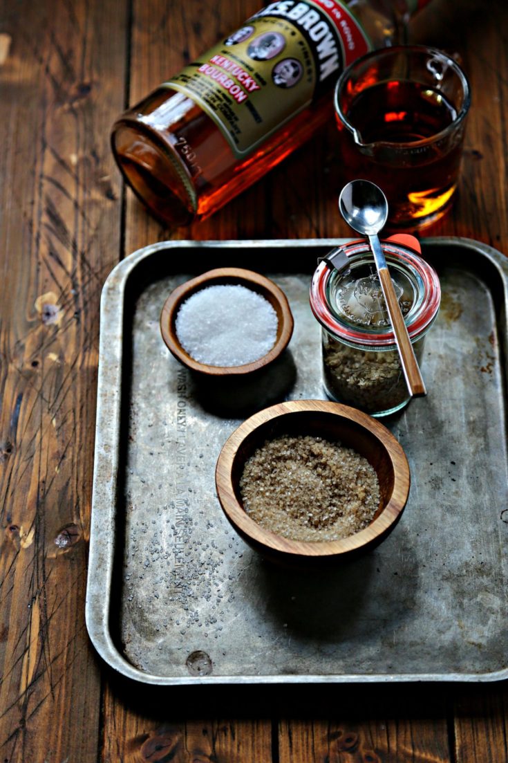 two bowls of salt, one glass jar of bourbon salt with spoon on baking sheet.