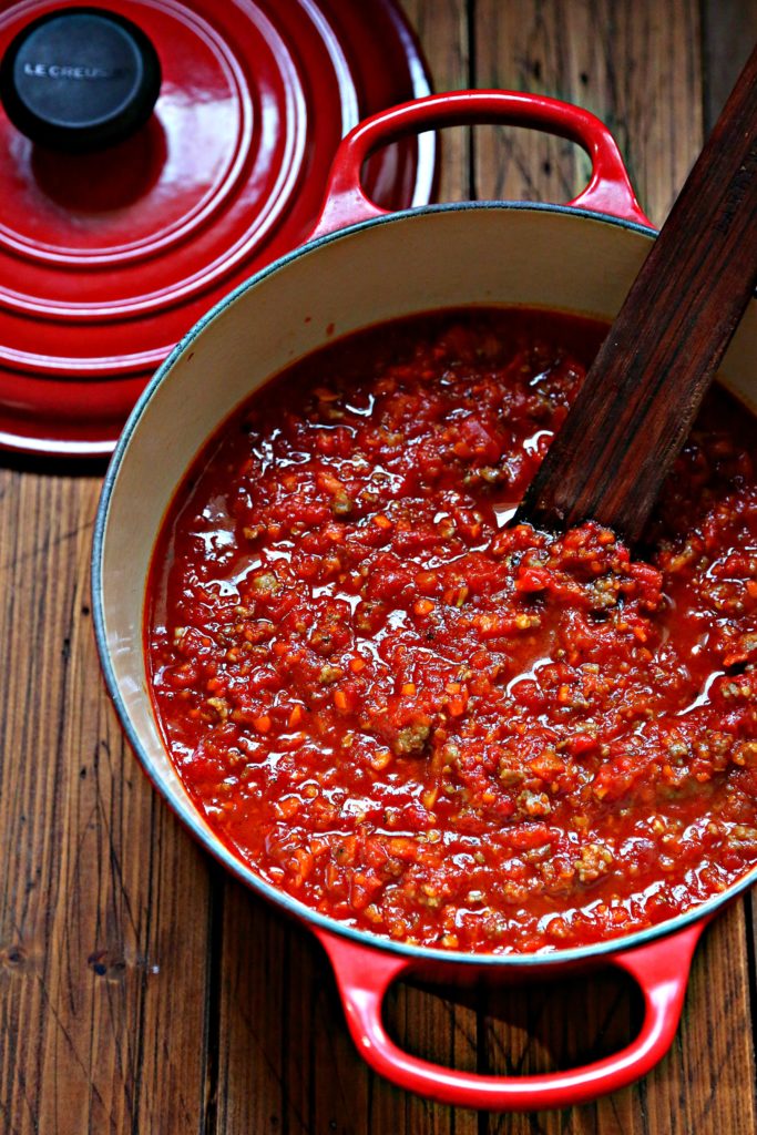 pasta sauce in red pot with spoon. Lid behind.