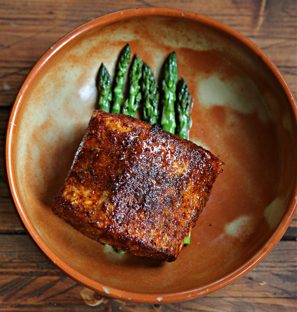 salmon over asparagus in brown bowl.
