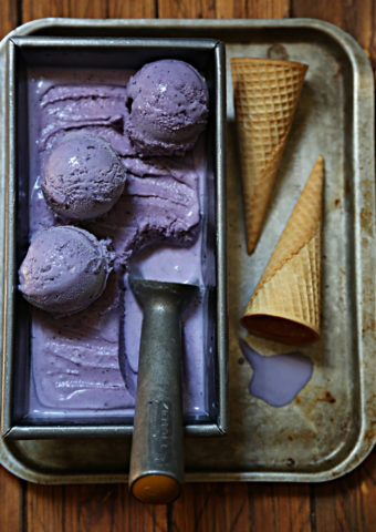 loaf pan of blueberry ice cream, scoop on top. 2 sugar cones to right of pan on baking sheet.
