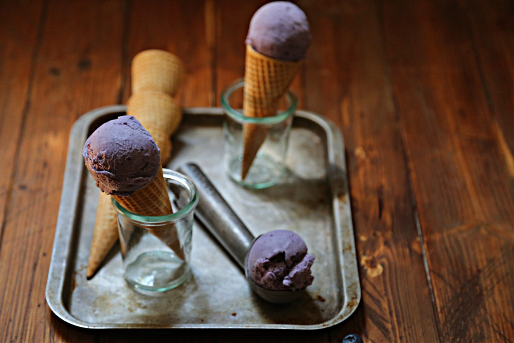 baking sheet with 2 ice cream cones in glass jars. Scooper of ice cream and stack of sugar cones.