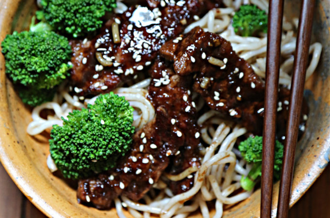 brown bowl with broccoli noodles and beef teriyaki. Chopsticks resting on bowl.