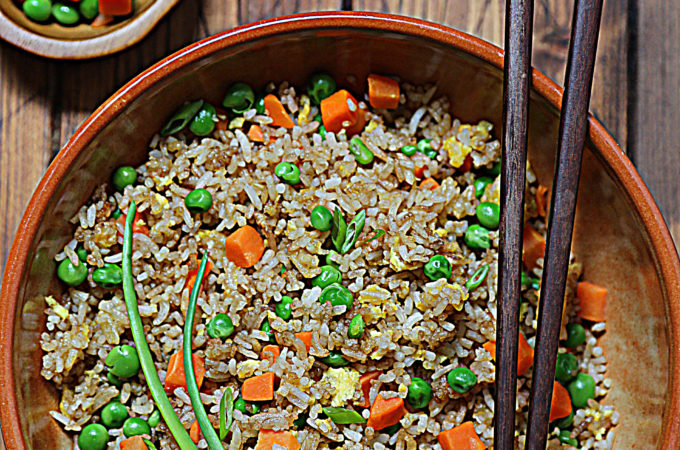 fried rice in brown bowl with chopsticks. Small bowl of vegetable blend to side.