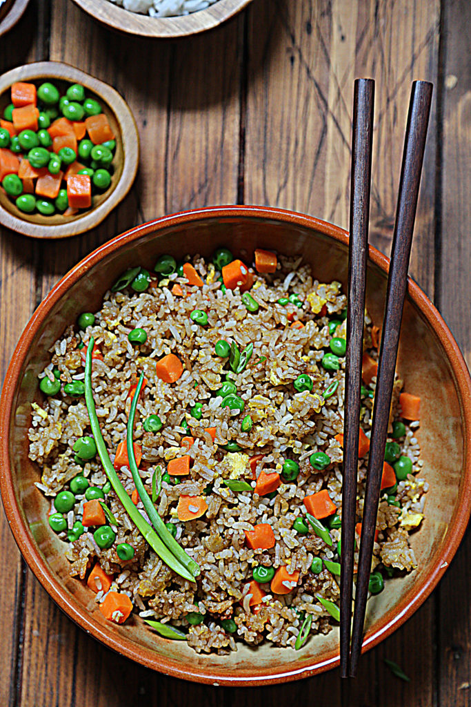 fried rice in brown bowl with chopsticks. Small bowl of vegetable blend to side. 