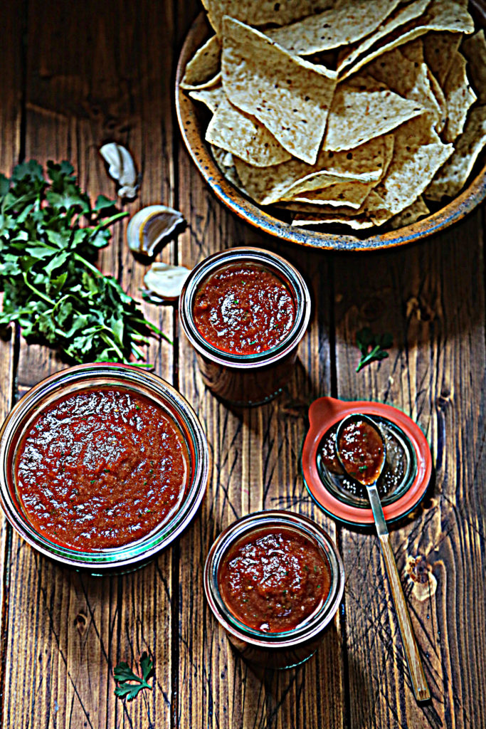 3 jars of red salsa. Chips, cilantro and garlic cloves around.