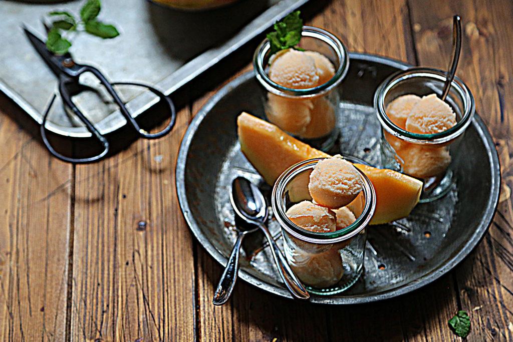 small jars filled with cantaloupe sorbet on metal tray with spoons.