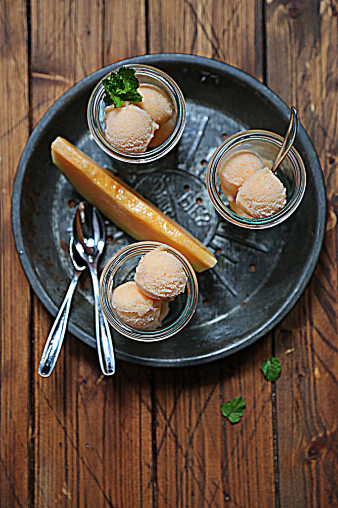 glass jars of sorbet on baking tin with spoons and slice of cantaloupe.