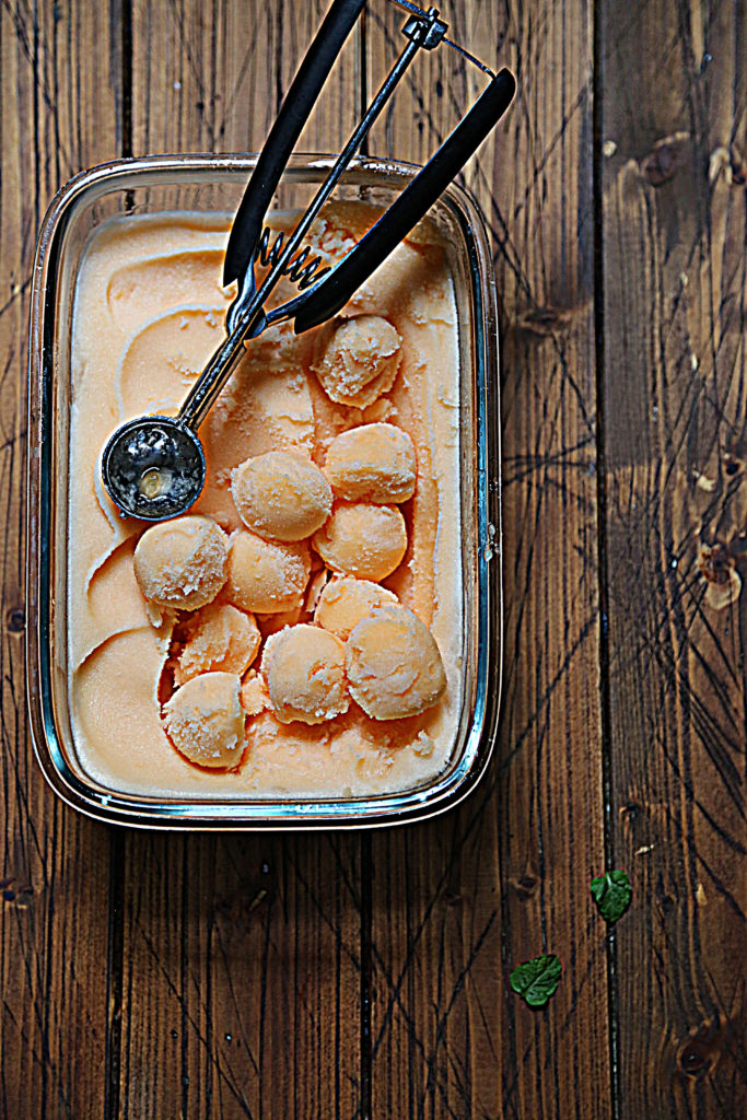 glass pan of cantaloupe sorbet with ice cream scoop. 
