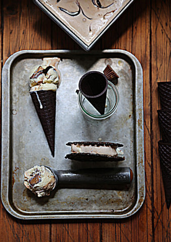 baking sheet with ice cream cone laying down, ice cream scooper with ice cream, ice cream sandwich and glass gar with ice cream cone standing.