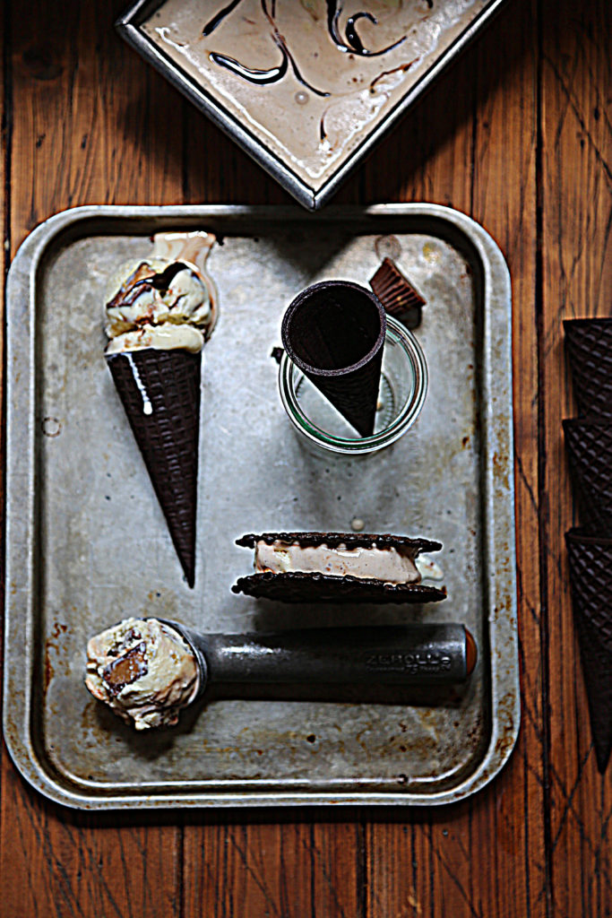 baking sheet with ice cream cone laying down, ice cream scooper with ice cream, ice cream sandwich and glass gar with ice cream cone standing. 
