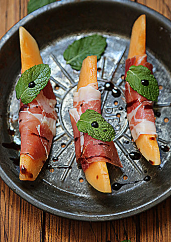 cantaloupe wedges wrapped in prosciutto on baking pan.