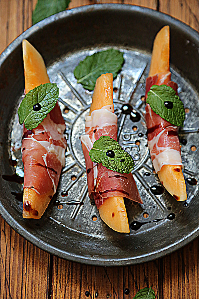 cantaloupe wedges wrapped in prosciutto on baking pan.