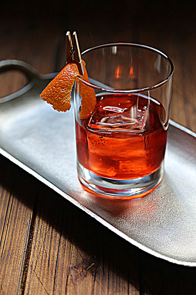 negroni cocktail with orange peel on silver tray.