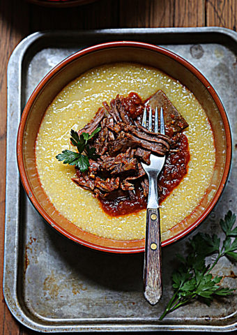 brown bowl with polenta and shredded short ribs with fork.