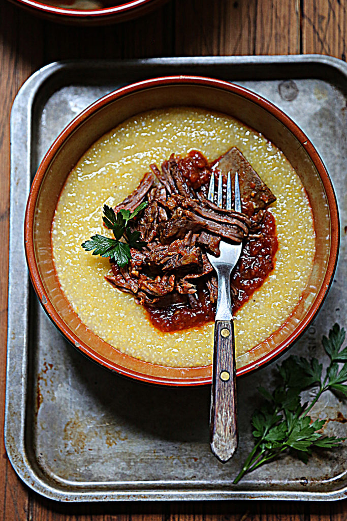brown bowl with polenta and shredded short ribs with fork. 