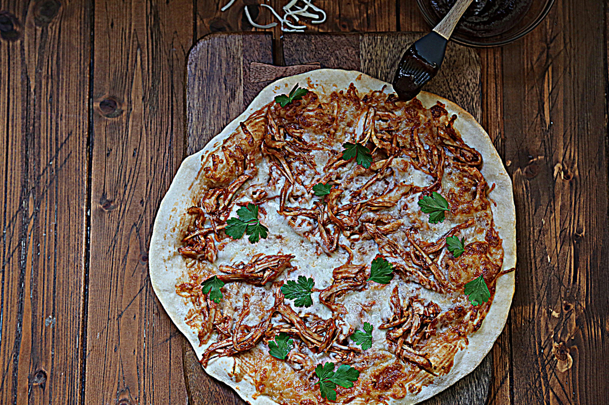 bbq turkey pizza on cutting board. Shredded mozzarella scattered behind pizza. 