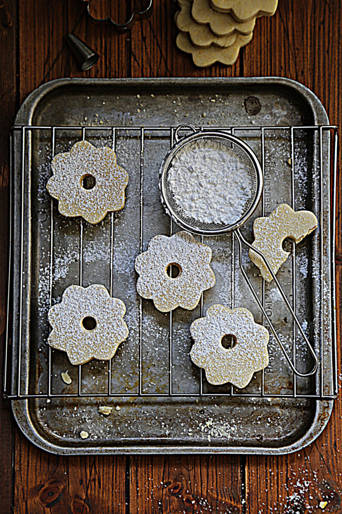 Cut out shortbread cookies on baking rack with sieve of powdered sugar.