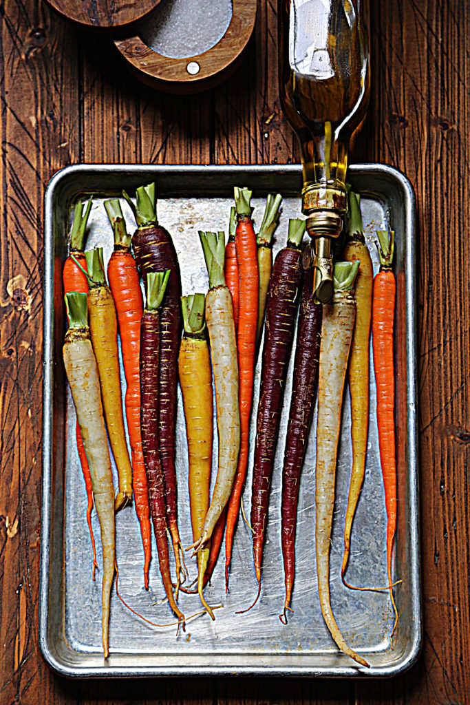 rainbow carrots on baking sheet with olive oil jar leaning over.