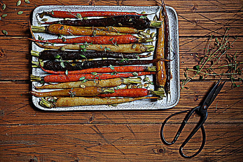 roasted rainbow carrots on platter. Scissors and herbs to side. 