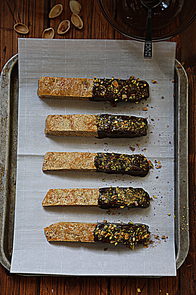 5 chocolate dipped biscotti sitting on baking sheet with parchment paper