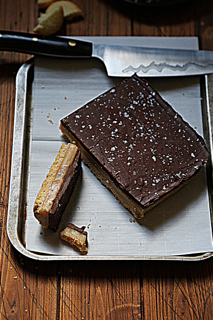 millionaire's shortbread sliced on baking sheet with parchment paper. Knife resting across baking sheet.