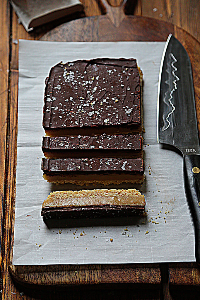 sliced millionaire's shortbread sitting on parchment paper, knife to side. 